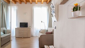 A modern living room with a wooden ceiling, a flat-screen TV on a cabinet, a sofa, and a cactus plant on a shelf. - Foresteria Della Corte (Como)