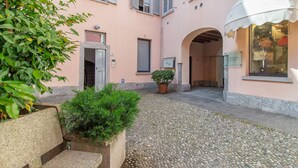 A courtyard with a stone bench, potted plants, and a building with a pink facade and arched entrance. - Foresteria Della Corte (Como)