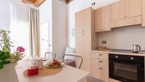 A modern kitchen with wooden cabinets, a built-in oven, and a dining area with a table set for two. - Foresteria Della Corte (Como)