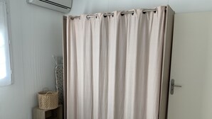 Ett badrum med en beige duschdraperi, en trähylla med en korg och en vit dörr.