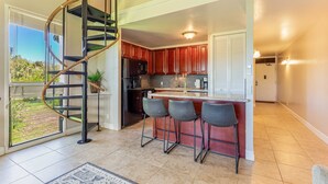 Une cuisine moderne avec un escalier en colimaçon, un coin bar avec des tabourets et une vue sur l’extérieur.
