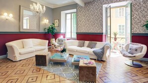 Een woonkamer met een beige bank, een witte fauteuil, een salontafel en een kamerbreed tapijt met een patroon.