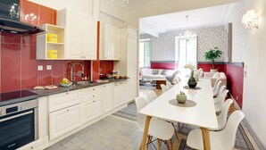 Een moderne keuken met witte kastjes, een zwarte afzuigkap en een eethoek met een witte tafel en stoelen.