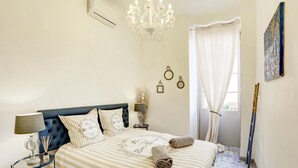 Een keurig opgemaakt slaapkamer met een bed, nachtkastjes, een kroonluchter en een raam met gordijnen.