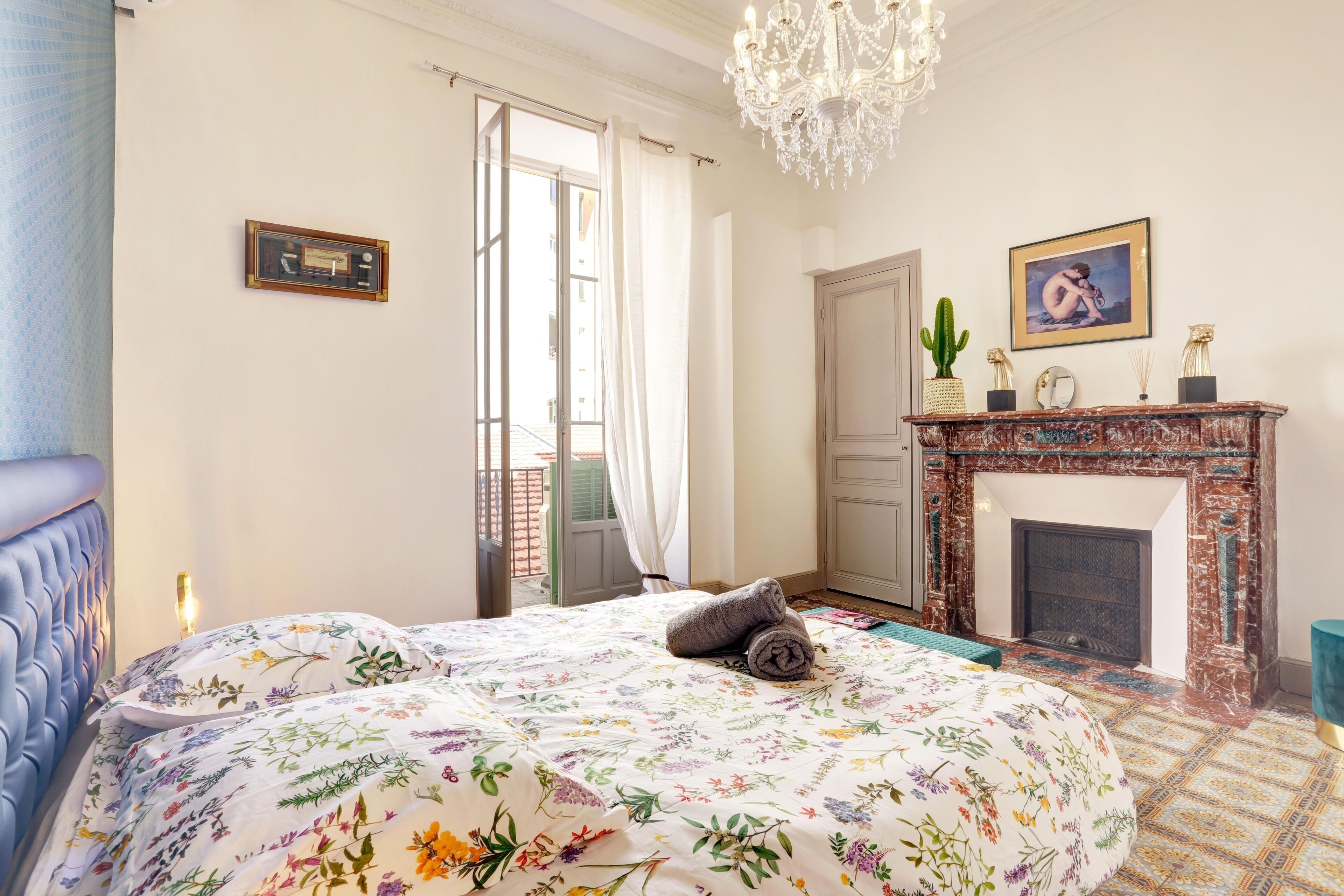 Een slaapkamer met een bed, een kroonluchter, een open haard en een deur die uitkomt op een balkon.