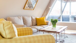 A modern living room with a sofa, yellow cushions, a coffee table, and a window with a view of buildings. - Large apartment - very illuminated, Wi-Fi, ocean view, close to the beach and ni (Wittdün)