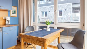 A modern room with a wooden table, chairs, a coffee machine, and a window with a view of a brick building. - Large apartment - very illuminated, Wi-Fi, ocean view, close to the beach and ni (Wittdün)