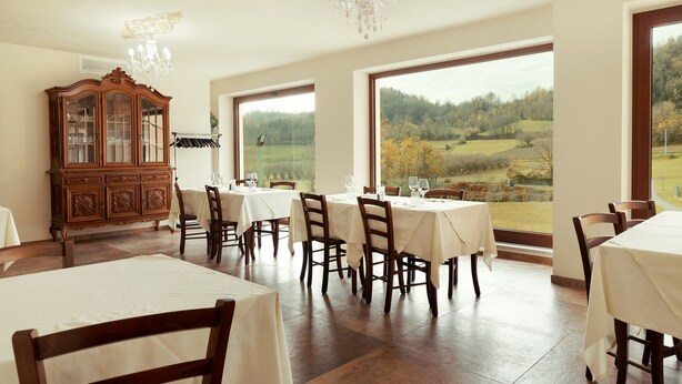 Comedor con mesas dispuestas para seis, un aparador de madera y vistas a un paisaje rural a través de grandes ventanales.