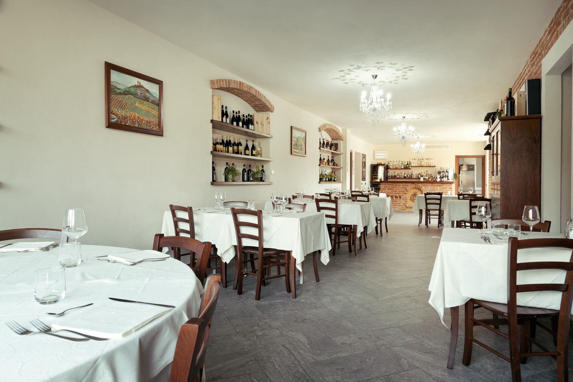 Ein Restaurant mit mehreren Tischen, gedeckt mit Besteck und Gläsern, und Regalen mit Flaschen im Hintergrund.