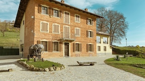 Un edificio de ladrillo de dos pisos con un patio empedrado de piedra, un barril antiguo y una banca.