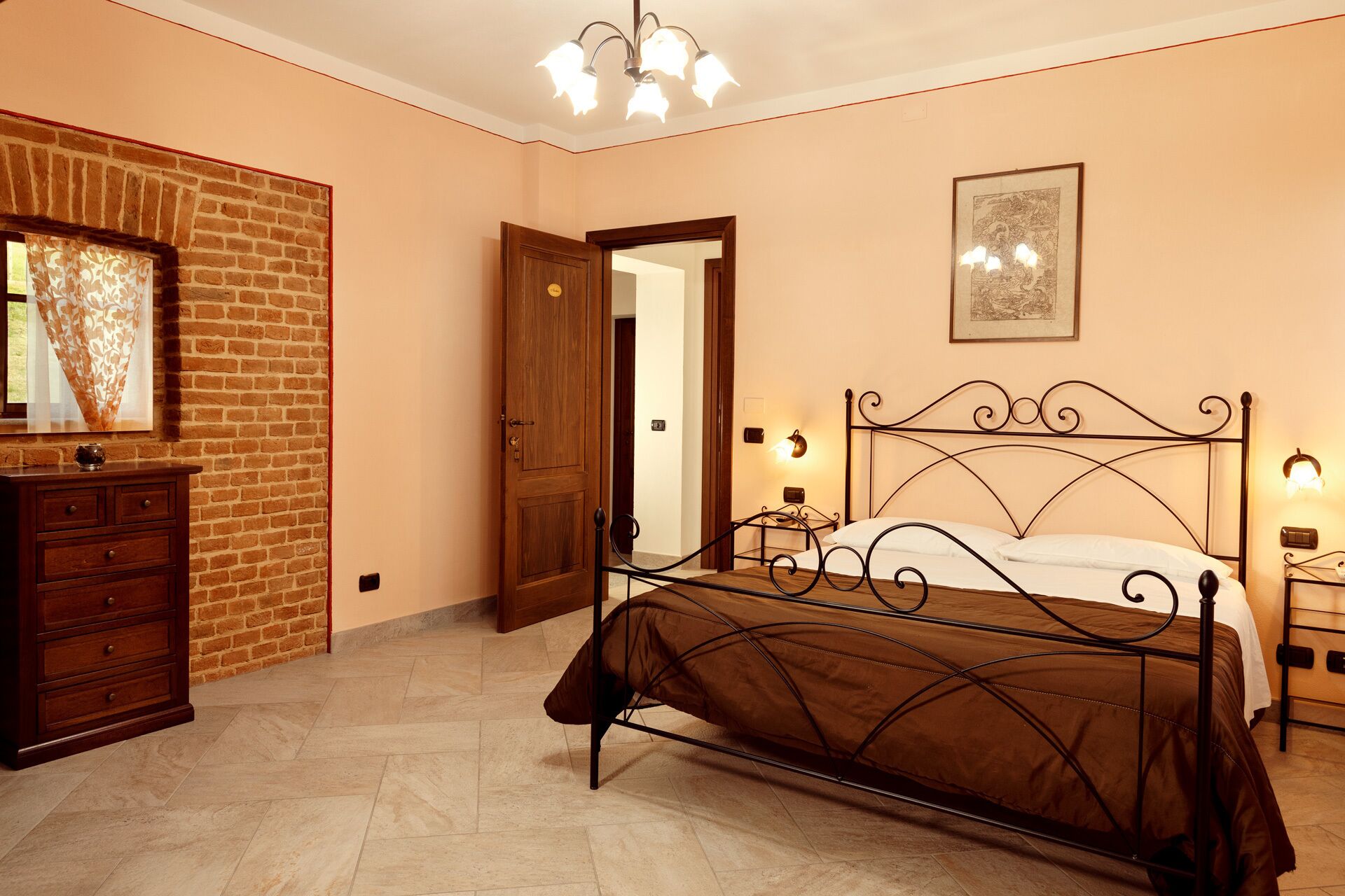 A bedroom with a brick wall, a wooden dresser, a metal bed frame, and a door leading to another room.