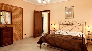 A bedroom with a brick wall, a wooden dresser, a metal bed frame, and a door leading to another room.
