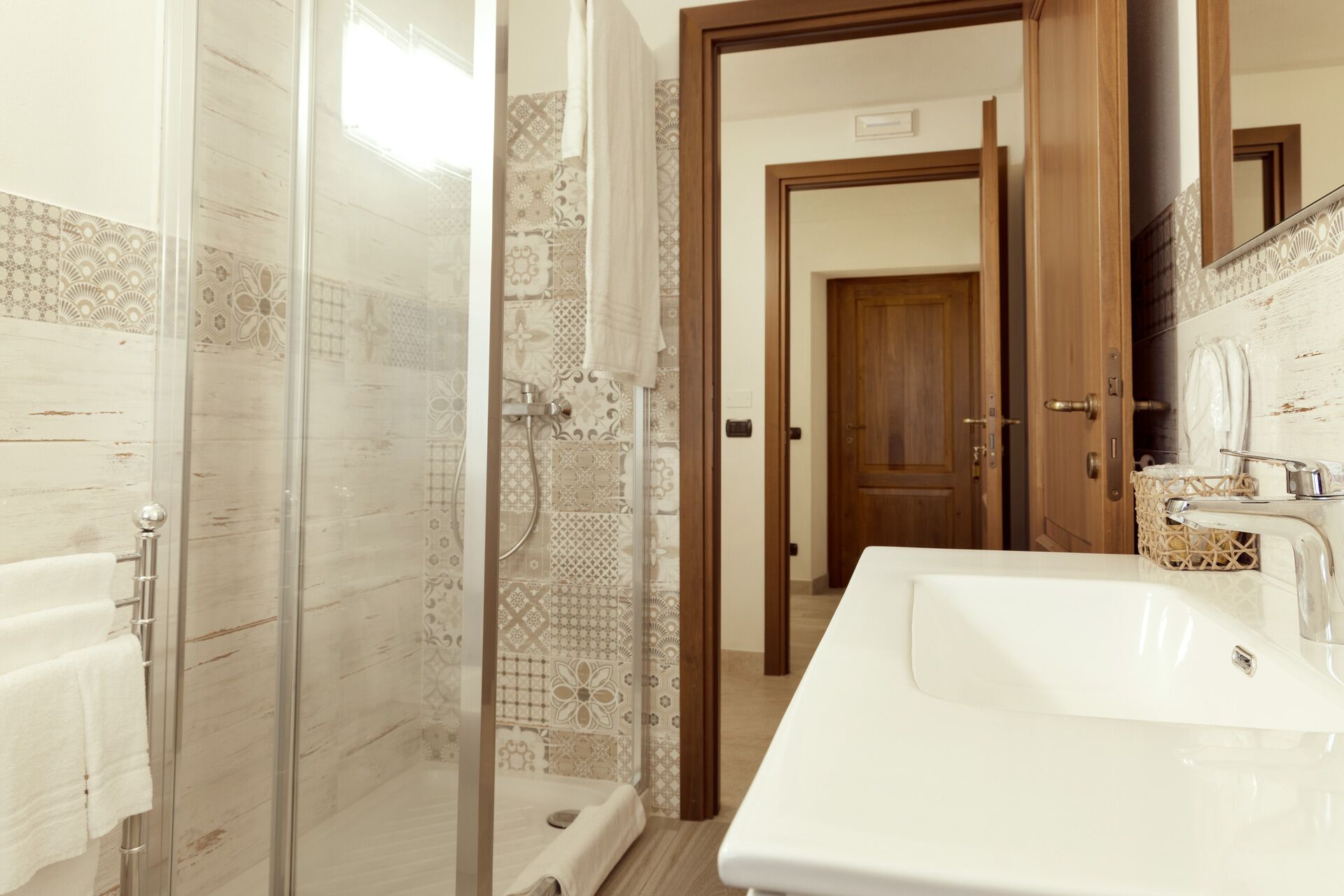 A bathroom with a glass shower enclosure, a white sink, and a wooden door in the background.