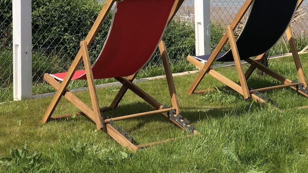 Twee strandstoelen op een gazon met uitzicht op de zee, met een straaljager in de verte.
