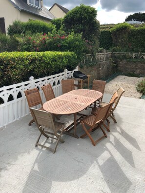 Un patio al aire libre con una mesa redonda de madera y seis sillas, rodeado por una cerca blanca de piquete.