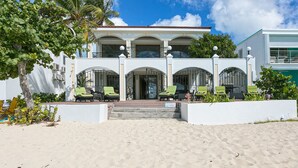A beachfront property with a white building featuring a balcony with green chairs.