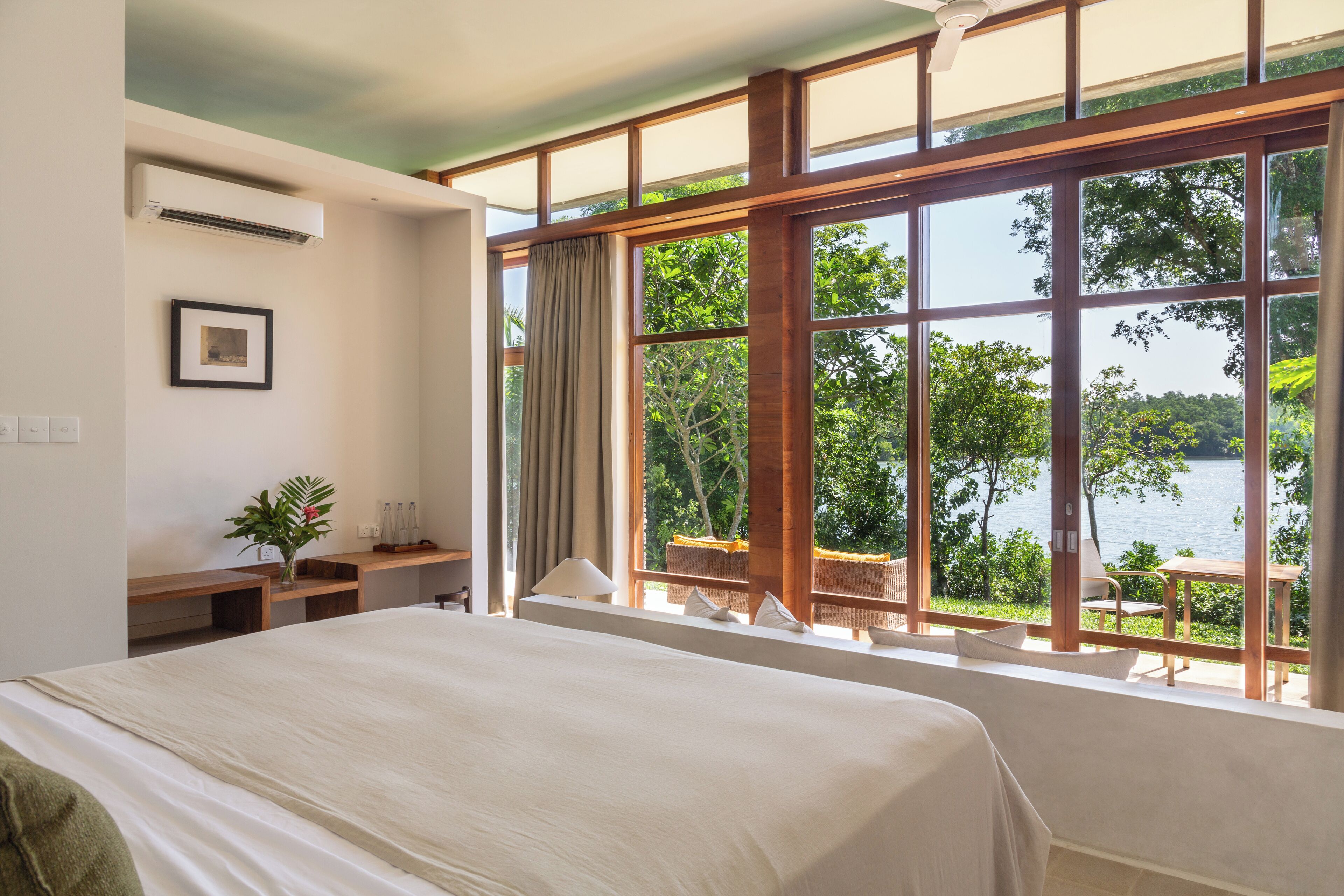 A hotel room with a large bed, a desk, and a view of a lake through large windows.