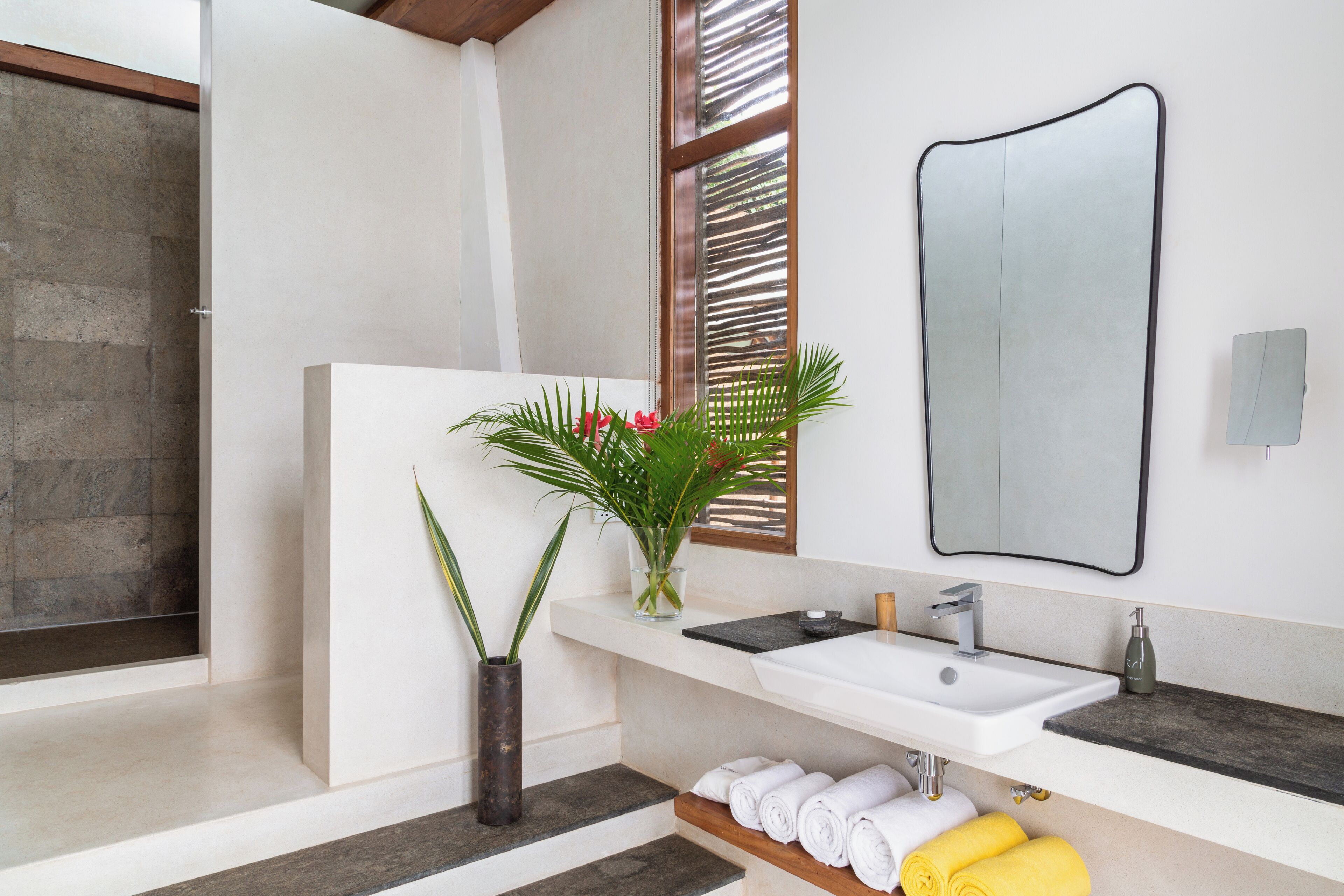 A modern bathroom with a large mirror, a white sink, and a shower area.