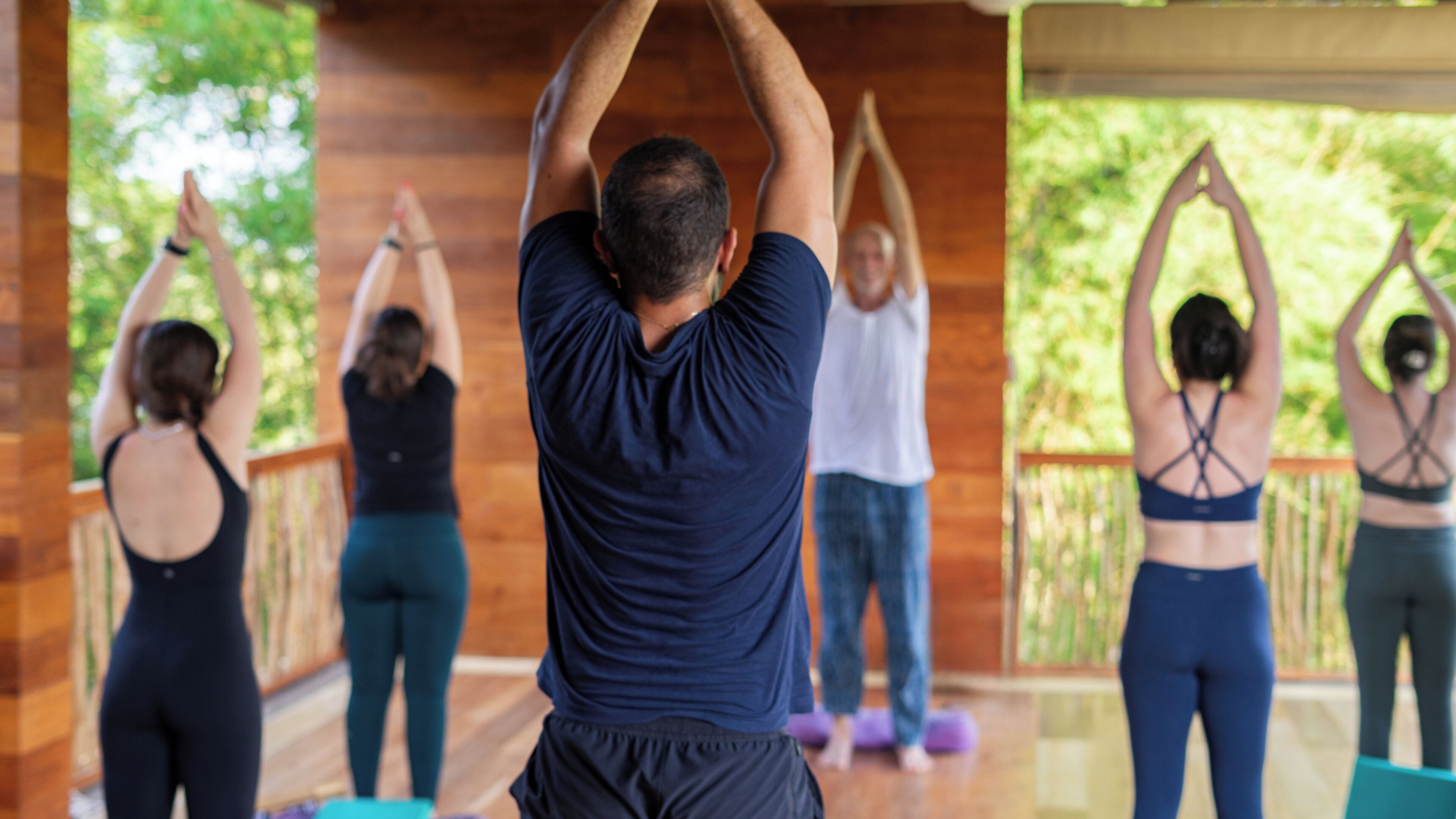 A group of people performing yoga on a wooden deck with a wooden railing.