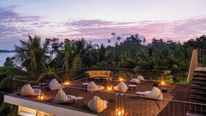 An outdoor seating area with a sofa, chairs, and cushions, surrounded by a railing, overlooking a body of water and palm trees. - Tri Ahangama (Ahangama)