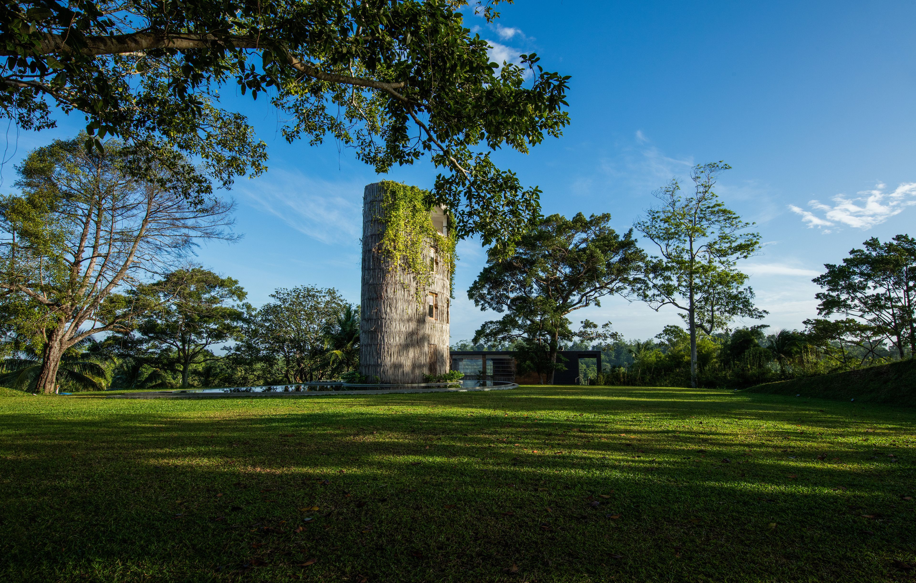 Une grande structure cylindrique en pierre, entourée d’une végétation luxuriante et d’arbres.