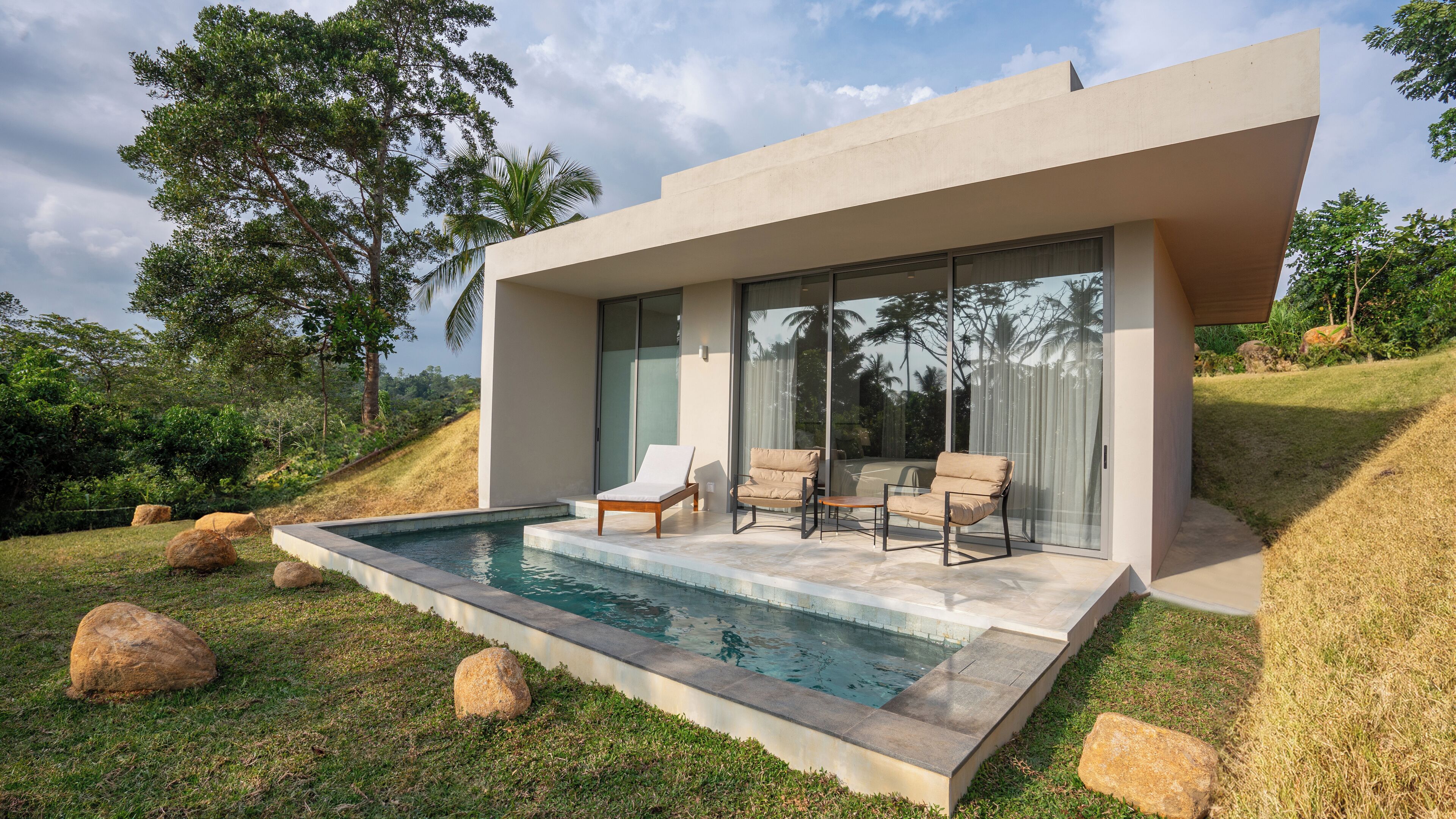 Una casa moderna con piscina, dos sillones de descanso y un gran ventanal.