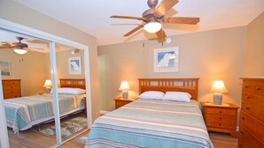 A bedroom with a large bed, two bedside tables with lamps, a ceiling fan, and a mirror. - Club Ocean Villas II 88-Bayside 120th St, WIFI, W/D, AC (Ocean City)