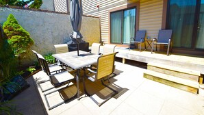 An outdoor patio with a table and chairs, a covered umbrella, and a wooden deck. - Club Ocean Villas II 88-Bayside 120th St, WIFI, W/D, AC (Ocean City)