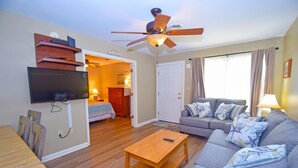 A living room with a wooden coffee table, a gray sofa with patterned cushions, a ceiling fan, and a flat-screen TV mounted on the wall. - Club Ocean Villas II 88-Bayside 120th St, WIFI, W/D, AC (Ocean City)