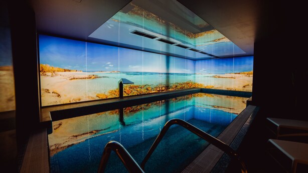 A modern indoor pool with a large window offering a view of a beach and ocean.