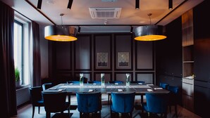 A dining area with a long table, blue upholstered chairs, and two pendant lights.