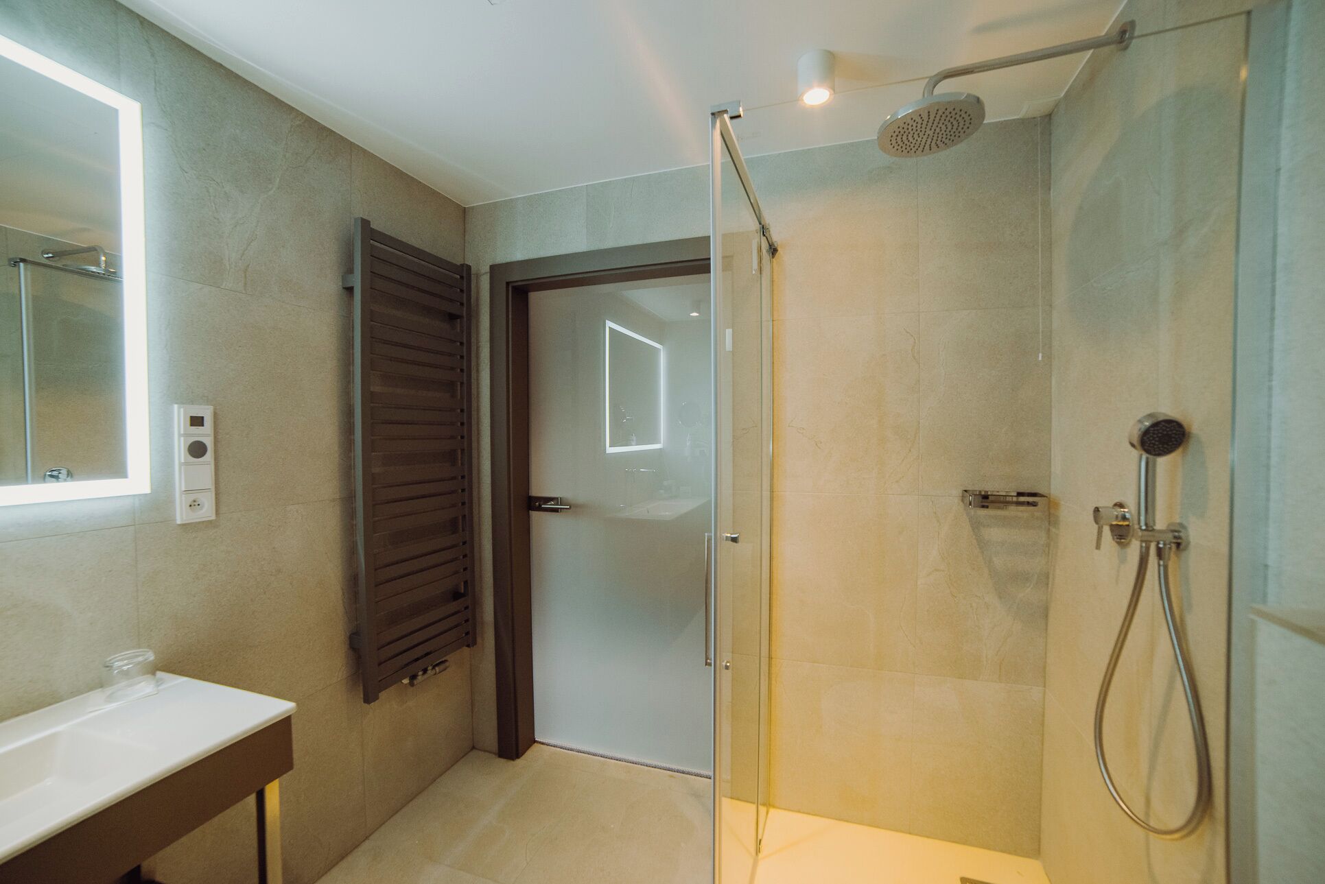 Un baño moderno con cabina de ducha de vidrio, un lavabo blanco y una puerta que da a otra habitación.
