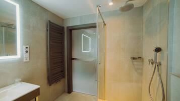 Un baño moderno con cabina de ducha de vidrio, un lavabo blanco y una puerta que da a otra habitación.
