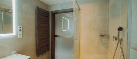 A modern bathroom with a glass shower enclosure, a white sink, and a door leading to another room.