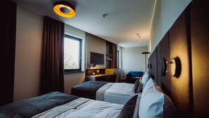 A hotel room with two beds, a desk, a chair, a TV, and a window.