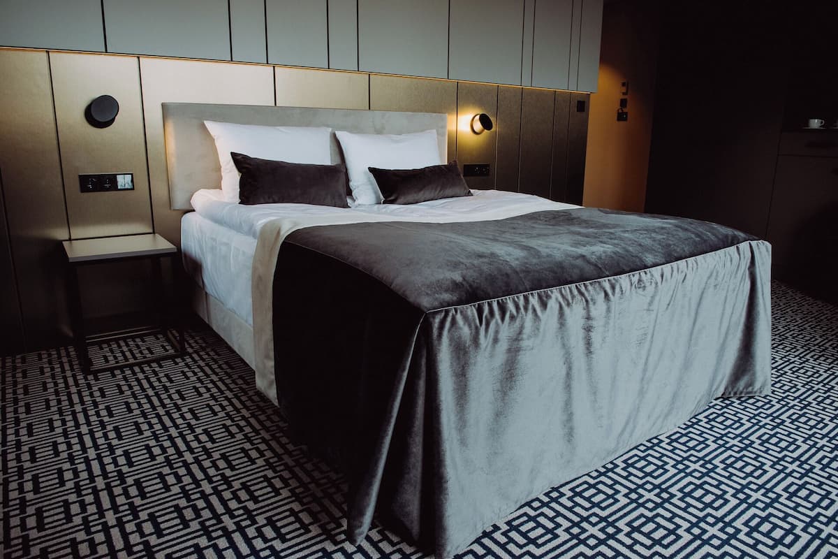 Una habitación de hotel moderna con una cama bien hecha, una mesita de noche y un suelo estampado.