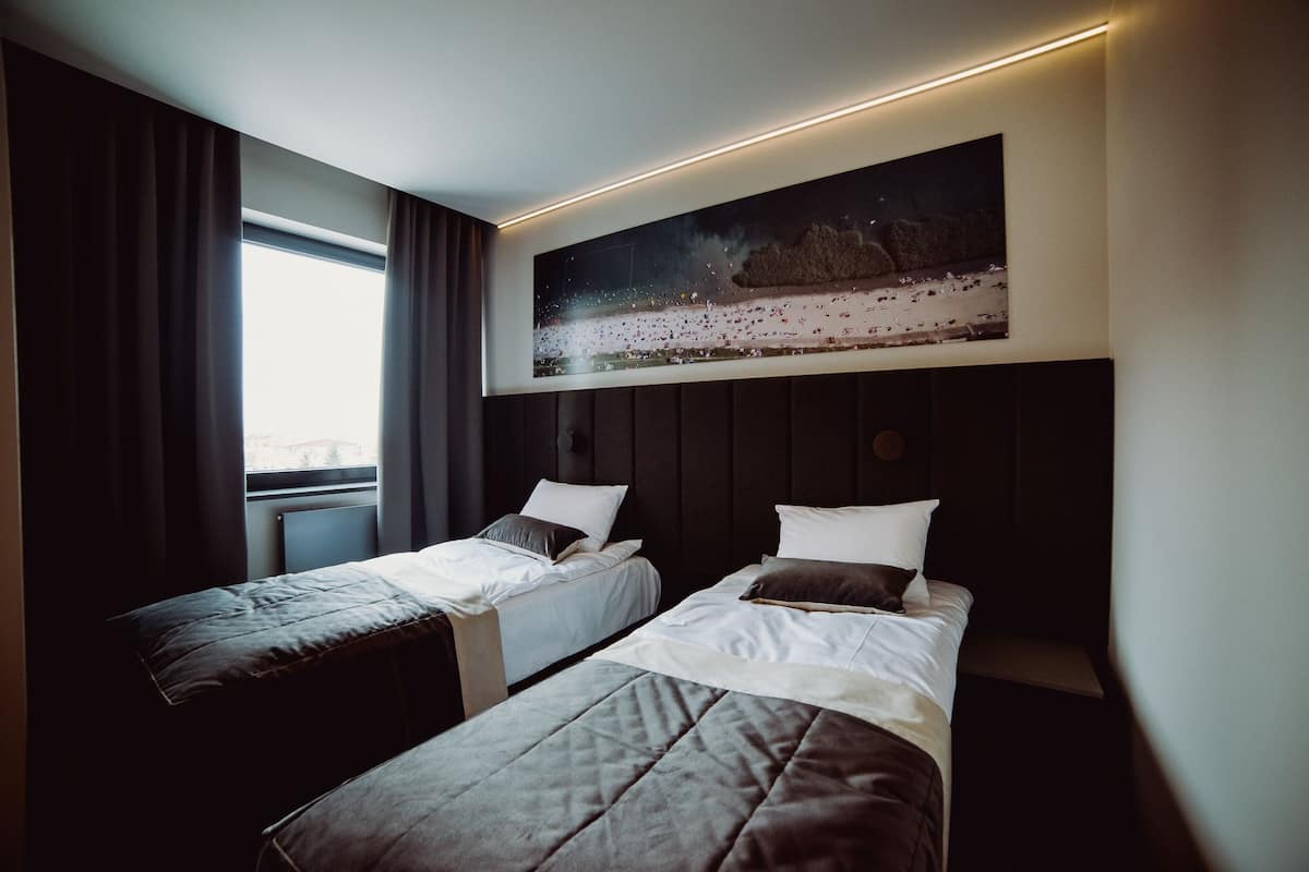 Habitación de hotel con dos camas, un cuadro grande sobre ellas y una ventana con cortinas.