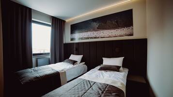 A hotel room with two beds, a large painting above the beds, and a window with curtains.