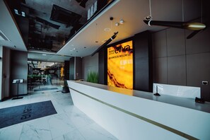 A hotel reception area with a modern design, including a reception desk, a digital display, and a view of the lobby. - Hotel Evva Business & Wellness (Tarnobrzeg)