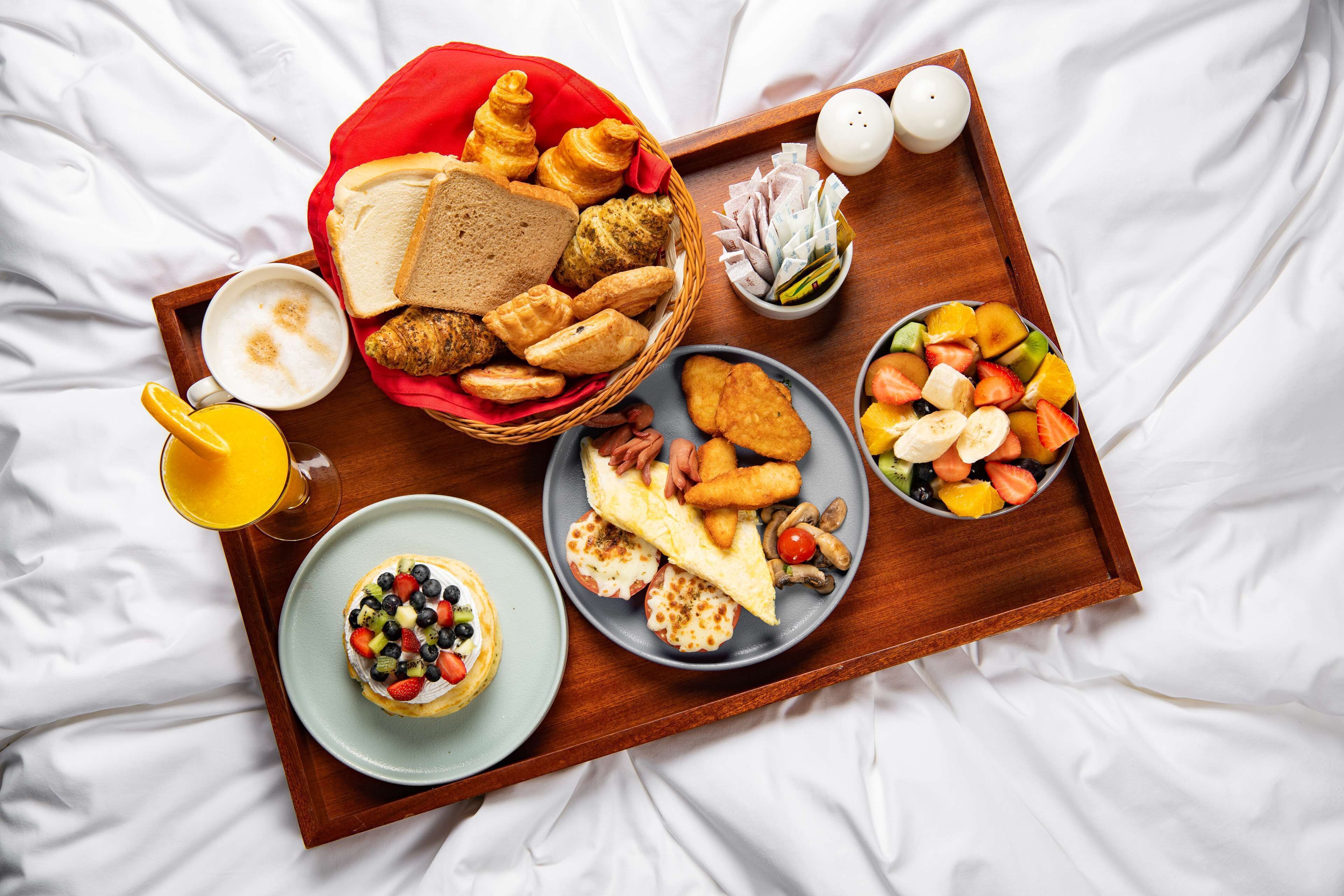 Un vassoio per la colazione con diversi cibi e bevande su un letto.