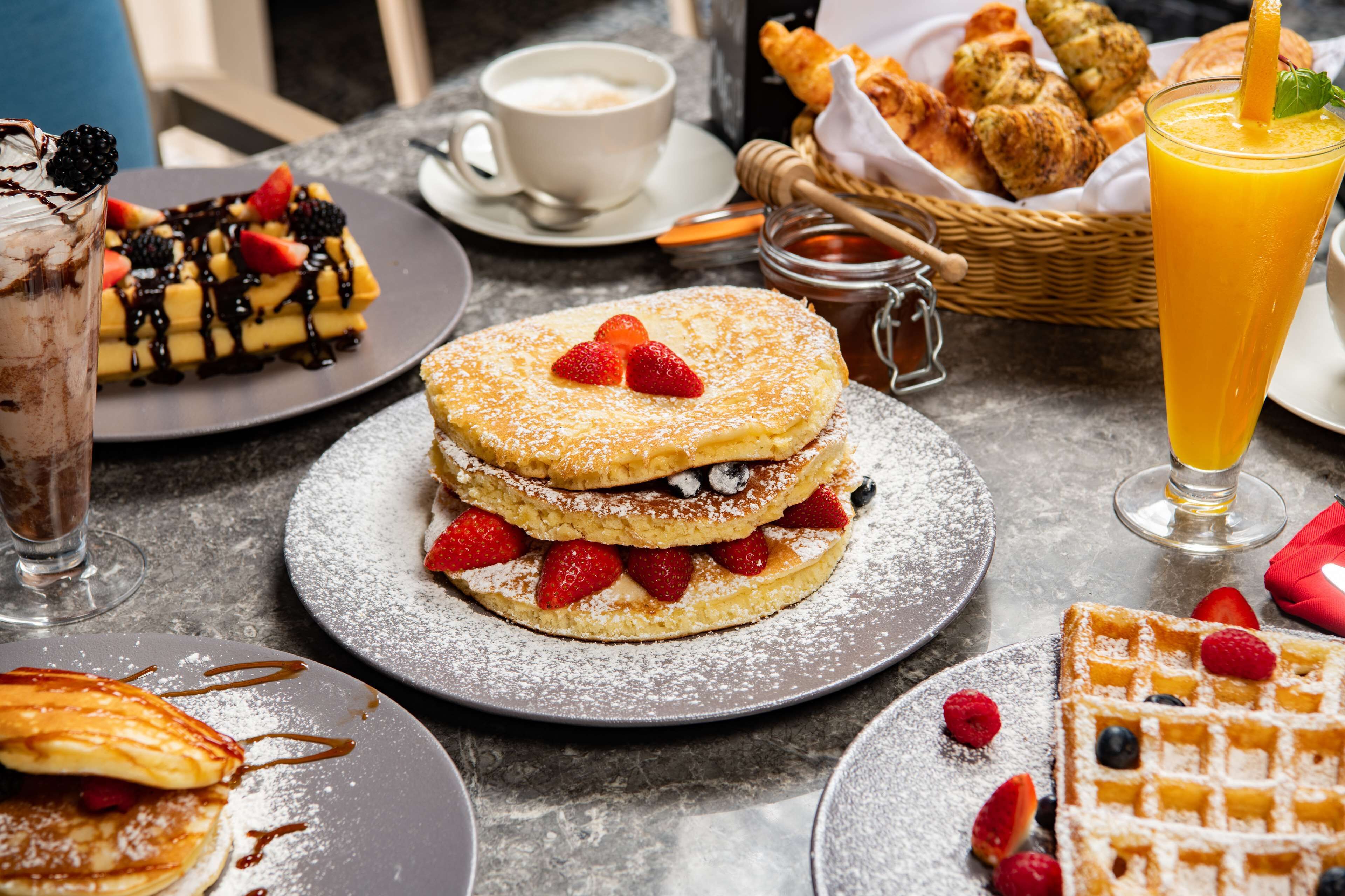 Mesa de café da manhã com waffles, panquecas e um copo de suco de laranja.
