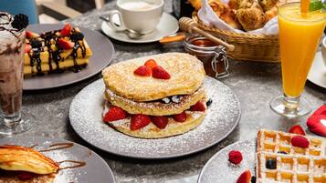 Mesa de café da manhã com waffles, panquecas e um copo de suco de laranja.