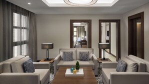 Una habitación de hotel moderna con un conjunto de sofá, una mesa de centro con objetos decorativos, una lámpara y un espejo grande.