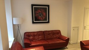 A living room with a red leather sofa, a framed picture on the wall, and a white door. - Chapel Apartments (Aberdeen)