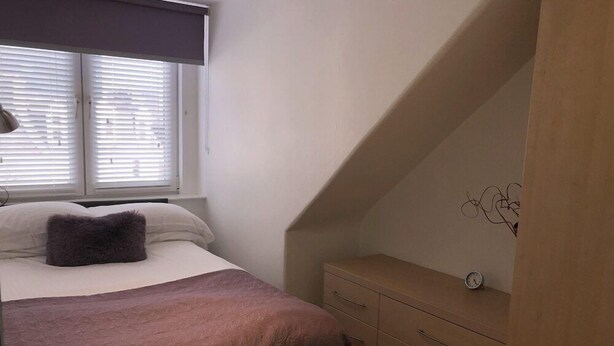 A bedroom with a bed, a dresser, and a window with blinds. - Chapel Apartments (Aberdeen)