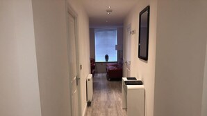 A narrow hallway with a radiator, a small white cabinet, and a red sofa in the background. - Chapel Apartments (Aberdeen)
