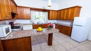 Eine Küche mit Holzausstattung, Granit Arbeitsplatten, einem weißen Kühlschrank und einem Fenster mit Vorhängen.