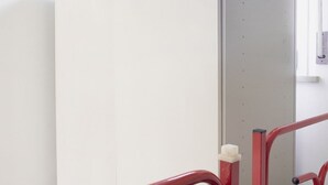 Een kamer met een witte muur, een rode metalen stoel en een deur met een handgreep.