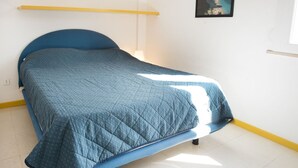 Een eenpersoonsbed met een blauw hoofdeinde en voeteinde, een gebogen blauwe deken en een witte muur met een ingelijste foto.