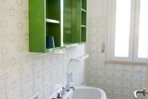 A bathroom with a white sink, green cabinets, and patterned tiles.